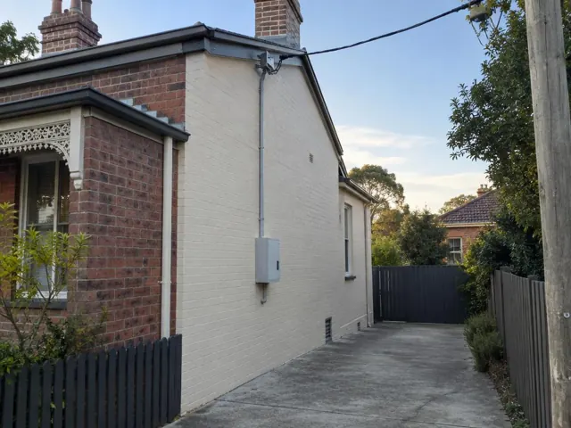 Overhead service cable and point-of-attachment on a brick and rendered house exterior in Annandale
