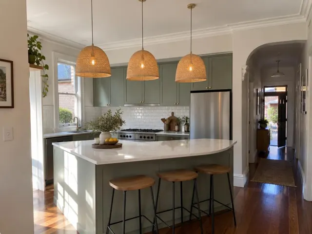 Kitchen with three woven pendant lights over a green island in a home in Stanmore