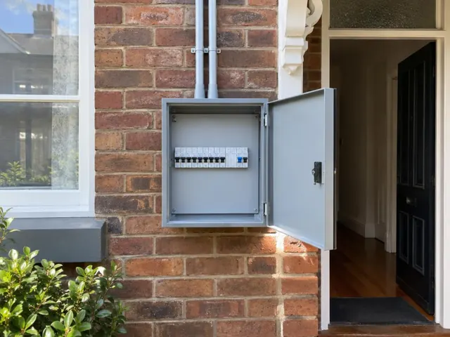 External switchboard cabinet mounted on a brick wall beside a front door in Leichhardt